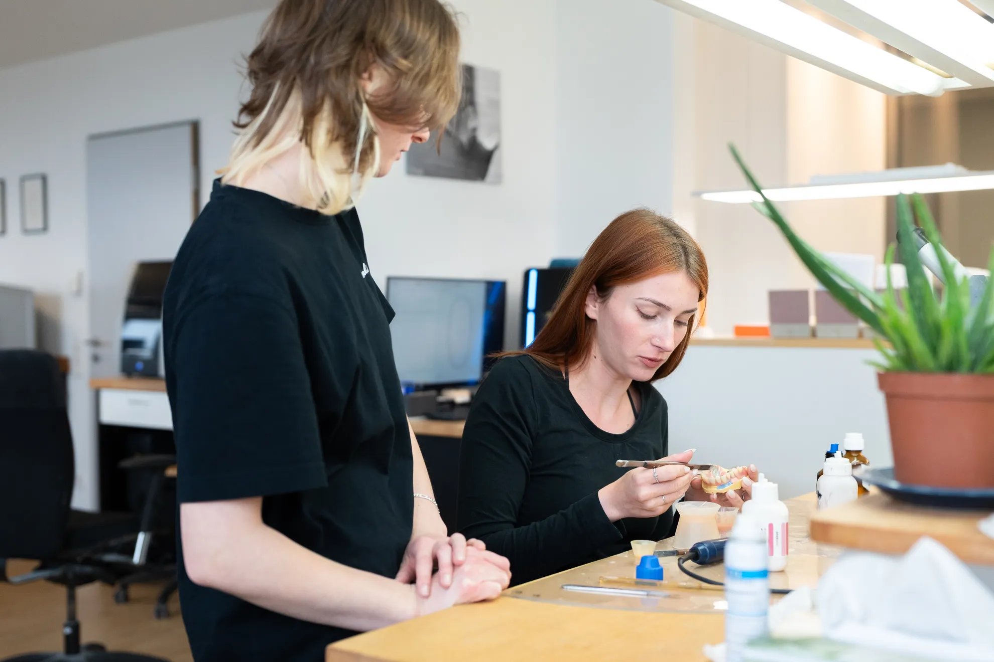 Eine Person arbeitet konzentriert an einem Modell, während die andere daneben steht und zuschaut
